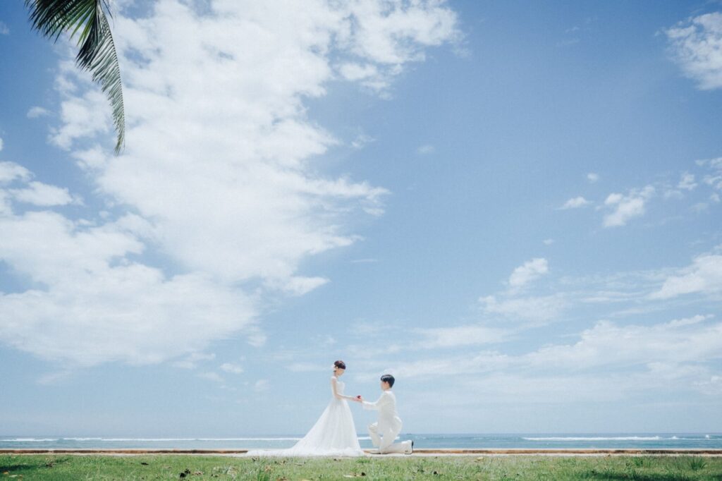 ハワイの青空とヤシの木の下で新郎がひざまずき新婦に指輪を捧げるプロポーズウェディングフォト